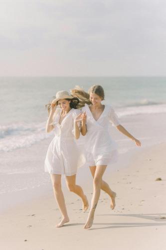 two women in white walking on the beach at Olhumathi View Inn in Ukulhas