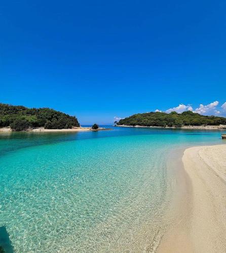 a beach with blue water and trees in the background at House Pollo in Ksamil
