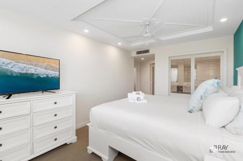 a white bedroom with a bed and a tv on a dresser at The Pool Resort Kingscliff - Private Apartments by Holiday Management Company in Kingscliff