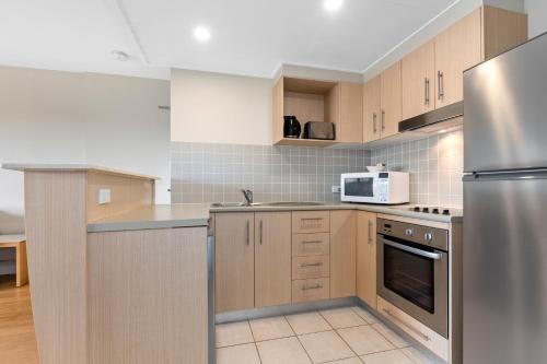 a kitchen with wooden cabinets and a stainless steel refrigerator at The Pool Resort Kingscliff - Private Apartments by Holiday Management Company in Kingscliff