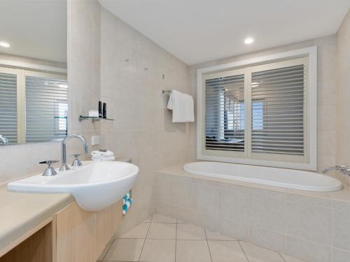 a bathroom with a sink and a tub and a window at The Pool Resort Kingscliff - Private Apartments by Holiday Management Company in Kingscliff