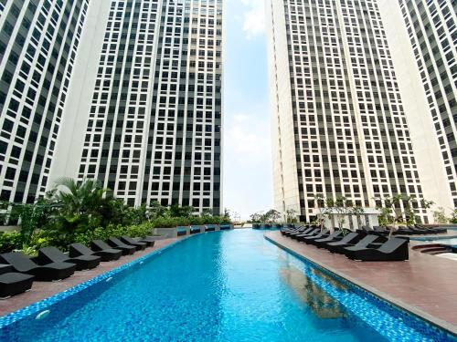 a swimming pool with chairs and two tall buildings at Simply and Comfortable 2BR Pollux Chadstone Apartment By Travelio in Cikarang