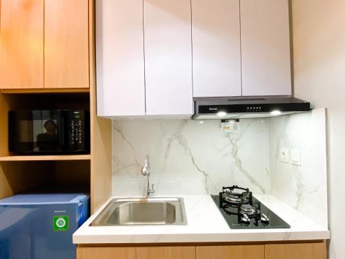 a kitchen with a sink and a microwave at Homey and Minimalist 1BR Vasanta Innopark Apartment By Travelio in Cikarang