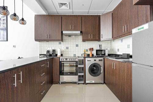a kitchen with wooden cabinets and a washing machine at Silkhaus Vacation Homes in Hydra Avenue Large Studio Near Reem Park in Abu Dhabi