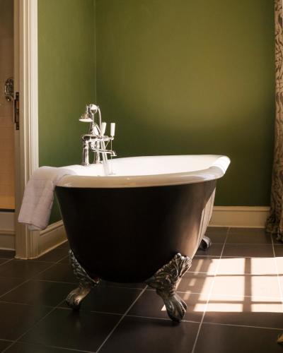 a bath tub in a bathroom with a green wall at Stoke Place- Part of the Cairn Collection in Slough