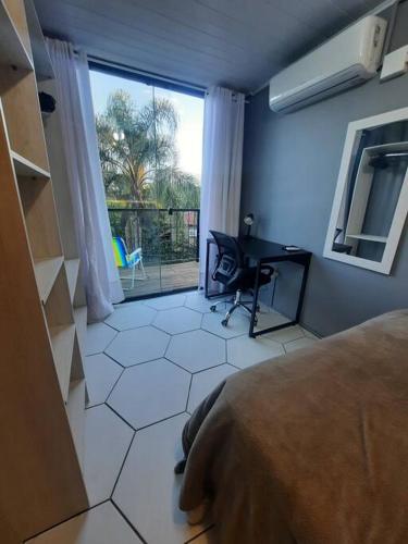 ein Schlafzimmer mit einem Bett, einem Schreibtisch und einem Fenster in der Unterkunft Apartamento Container com Sacada, Split e Estacionamento in Canoas