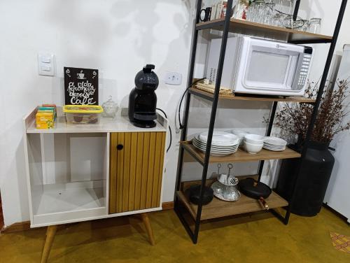 a kitchen with a microwave and a shelf with dishes at Casa Cipreste no Refúgio Pinheiro Beira Rio in Sapucaí-Mirim