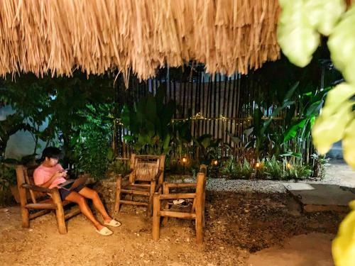 a man sitting in a chair under a straw umbrella at Jaydy hostel in General Luna