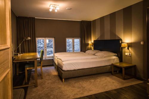 a bedroom with a bed and a desk and windows at Hotel De Limbourg in Sittard