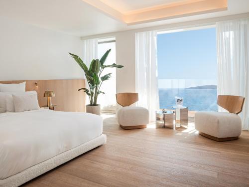 a bedroom with a bed and two chairs and a large window at The Roc Club, A Grecotel Hotel to Live in Athens