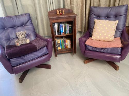 a teddy bear sitting in two chairs next to a book shelf at Silver Gum House in South Fremantle