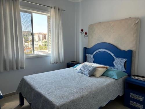 a bedroom with a bed with a blue headboard and a window at Apartamento Central Sétimo Andar in Serra Negra