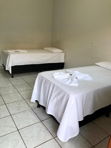 two beds with white sheets in a room at Hotel 2 Irmãos in Campo Grande