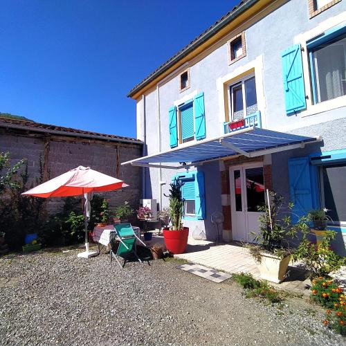 a house with an umbrella and a chair and a table at Chez Anne et Christian in Saint-Bertrand-de-Comminges