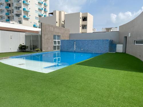a swimming pool with green grass in front of a building at Vista a Playa con Alberca en Blvd principal frente al Mar 3hab in Boca del Río