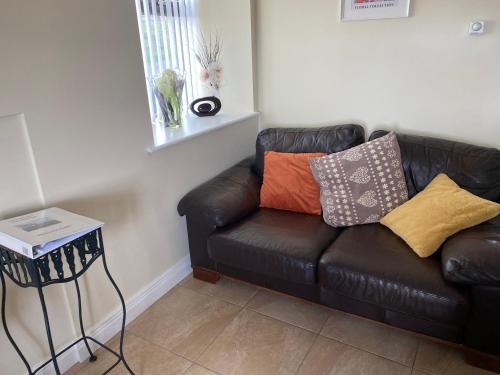 a black leather couch with colorful pillows on it at Greenridge Farmhouse in Crossmaglen