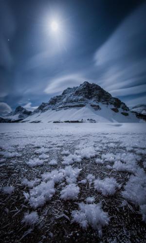 a mountain covered in snow with the moon in the sky at The Lodge at Bow Lake in Lake Louise