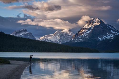 a person standing on the shore of a lake with a mountain at The Lodge at Bow Lake in Lake Louise