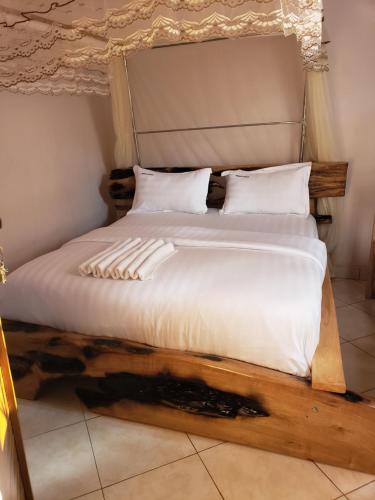 a bed with a wooden frame and white sheets and pillows at Mosai grill bar, restuarant and Accommodation in Entebbe