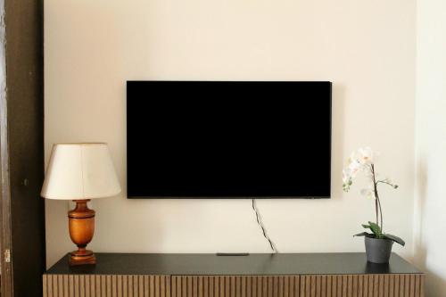 a television on a wall with a lamp and a flower at Dragonetti Luxury House in LʼAquila