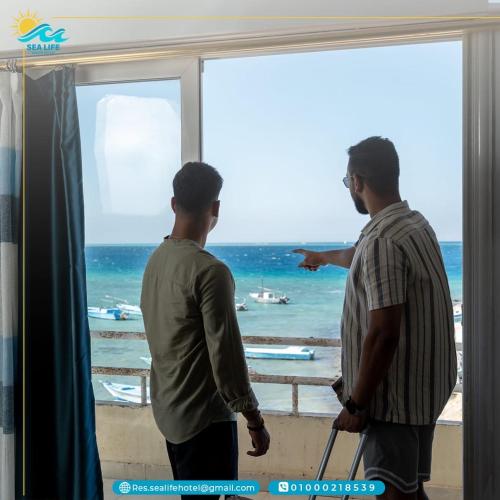 two men looking out of a window at the ocean at Sea Life Apartments-hotel in Hurghada