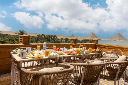 Una mesa con comida en un balcón con pirámides al fondo. en Taj Pyramids inn - Pyramids View Rooftop, en El Cairo