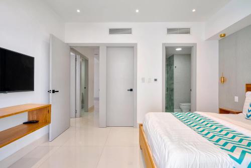 a white bedroom with a large bed and a flat screen tv at Monaco Residences Piantini in Santo Domingo