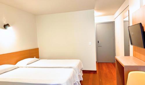 a hotel room with two beds and a flat screen tv at Hotel Atlântico in Guarapari