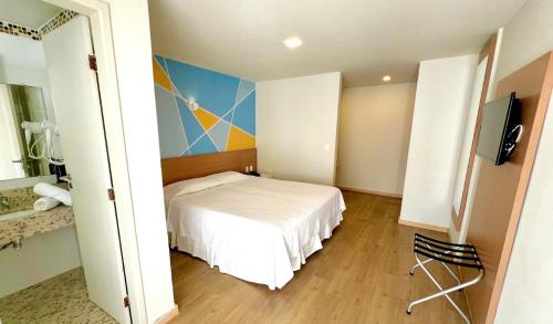 a bedroom with a white bed and a television at Hotel Atlântico in Guarapari