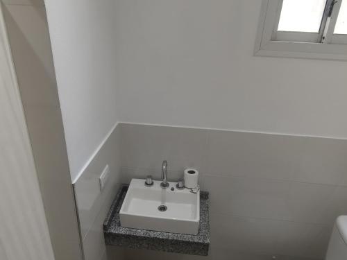 ein weißes Waschbecken im weißen Badezimmer mit Fenster in der Unterkunft Kuka 5 in Villa Gesell