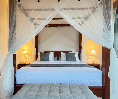 a bedroom with a large white bed with curtains at Alam Petanu in Ubud