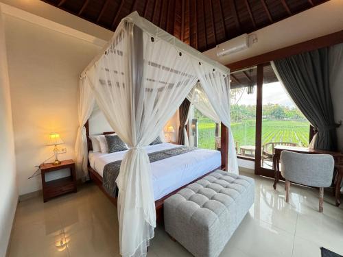 a bedroom with a canopy bed and a chair at Alam Petanu in Ubud