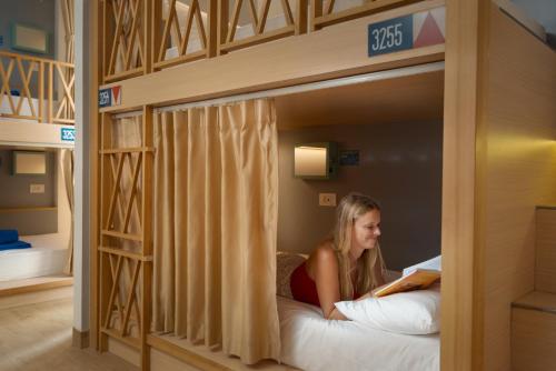 a woman sitting in a bunk bed reading a book at Lub d Siem Reap - Near Pub Street & Angkor Wat in Siem Reap