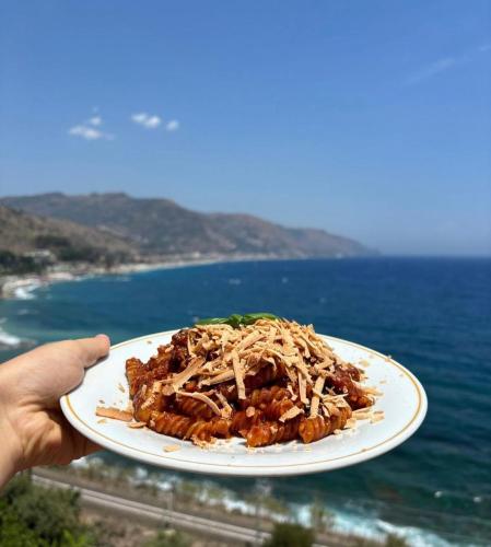 a person holding a plate of food with the ocean at Bay Palace Mazzarò in Taormina