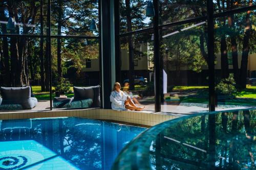 two women sitting next to a swimming pool in a building at Gabija Hotel SPA & Conferences in Palanga