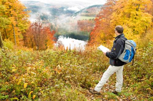 a man with a backpack standing on a hill looking at a valley at Ferienhaus Glücksnest in Hetzerath
