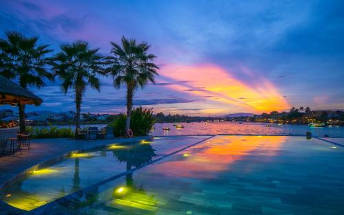 a swimming pool with palm trees and a sunset at Hoi An Memories Resort & Spa in Hoi An