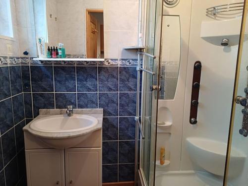 une salle de bain carrelée bleue avec un lavabo et une douche dans l'établissement Maison avec terrasse Merlimont Plage, à Merlimont