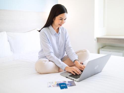 a woman sitting on a bed using a laptop computer at HOP INN Krabi Building A in Krabi town