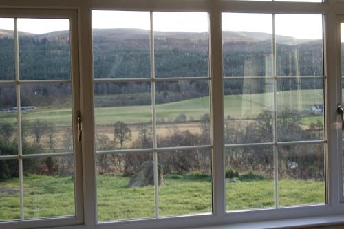 a view through a window of a large open field at BCC Loch Ness Cottages in Drumnadrochit