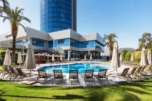 a pool with chairs and umbrellas in front of a building at Wyndham Grand Izmir Ozdilek Thermal & Spa in Izmir