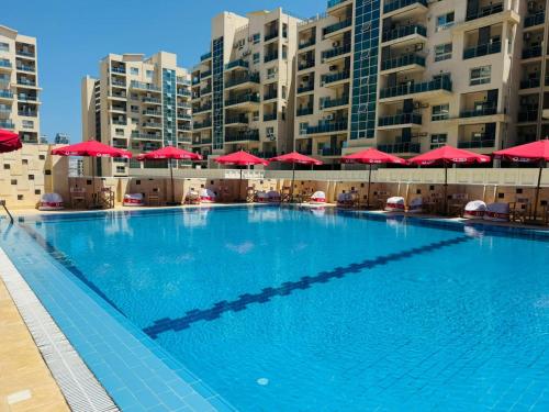 a large swimming pool with red umbrellas and buildings at Apartment at El Down Town New El Alamein in El Alamein