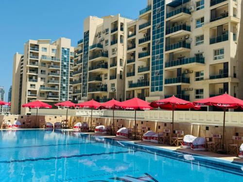 a swimming pool with red umbrellas and chairs and buildings at Down Town New ELalamein خلف الابراج وبجوار فندق ريكسوس العلمين in El Alamein