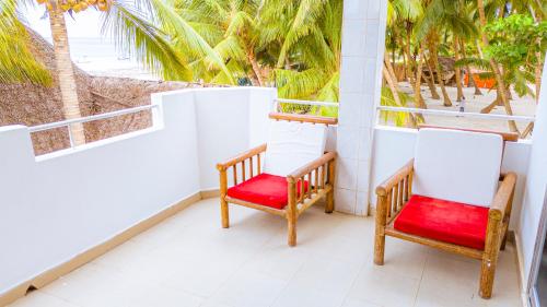 two chairs sitting on a balcony with palm trees at Sands Inn Hotel in Pwani Mchangani