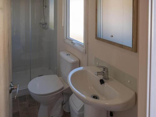 a bathroom with a toilet and a sink and a mirror at Pinewoods Park Classic 5 sleeps 6 – dog friendly in Wells next the Sea