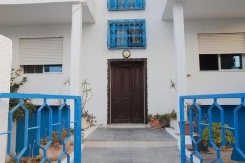 a white house with a brown door and blue gates at Maison bleue in Dar Salah Bey