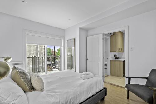a white bedroom with a large bed and a chair at Renovated 2-Bedroom Haven by Jean Talon Market in Montréal