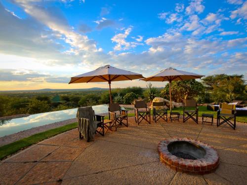 a patio with tables and umbrellas and a fire pit at Otjiwa Mountain Lodge in Otjiwarongo