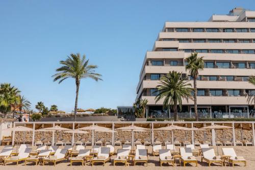 a beach with chairs and palm trees and a building at ME Sitges Terramar in Sitges