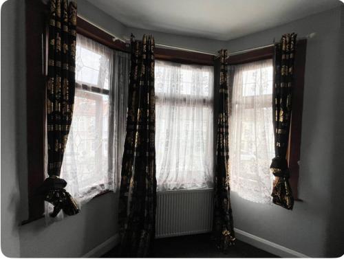 a room with two windows with curtains on them at EQU London in Ilford